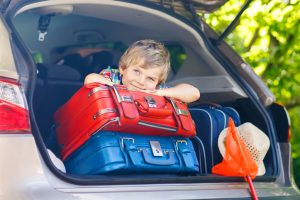 Adorable little kid boy sitting in car trunk just before leaving for summer vacation with his parents. Happy child with suitcases and toys going on journey. happy family traveling. Summer travel.